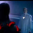 Zwei Personen in einem futuristischen Raum, eine mit roten Lichtern, die andere mit weißem Symbol auf der Brust.