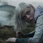 Eine Person mit blonden Haaren liegt alarmiert am Boden vor verschwommenem Hintergrund.