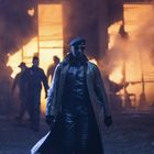 "NCG" auf einem Lastwagen. Person in Lederkleidung und Mütze vor Flammenkulisse inmitten von Rauch und weiteren Gestalten.