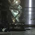 In einem düsteren Raum steht eine leuchtende Skulptur; links knien zwei Personen, rechts steht eine Person mit ausgestreckten Händen.