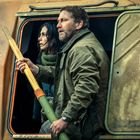 Nur teilweise lesbarer Text: "SAFELAUNCH, GEAR". Ein Mann und eine Frau schauen aus einem orangen Fahrzeug. Der Mann hält einen gelben Stab.