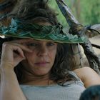 Ein Mensch mit einem aus Blättern geflochtenen Hut sitzt nachdenklich in einer natürlichen Umgebung.