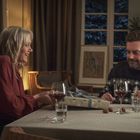 Ein Mann und eine Frau sitzen an einem Tisch mit Weingläsern, in gemütlicher Atmosphäre, lächeln und unterhalten sich.