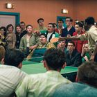 An einer Tischtennisplatte versammeln sich viele junge Erwachsene in lebhafter Kleidung, im Spiel vertieft.