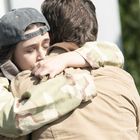 Ein Parkverbotsschild im Hintergrund. Zwei Personen, eine mit Camouflage-Jacke, umarmen sich innig.