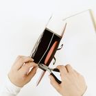 Zwei Hände arbeiten mit einer Zange an einem Bastelprojekt mit Karton und Draht.