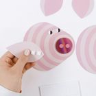 Ein Schweinsgesicht aus Papier mit rosa Streifen. Hand hält Papierohr mit Klebepunkten.