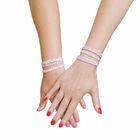 Zwei Hände mit bunten Armbändern und rot-pink lackierten Nägeln, überschneiden sich elegant vor hellem Hintergrund.