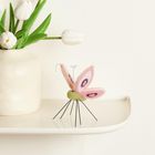 Keine Texte. Eine vaas mit weißen Tulpen und eine filigrane, bunte, textile Insekten-Skulptur auf einem Regal.