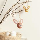 Drei Filzhasenköpfe hängen an Zweigen über einem Korb mit weißen Eiern.