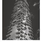 "12" und Zahlen von 1 bis 31. Schwarz-weiß Foto eines modernen, stufenartig gebauten Hochhauses vor wolkigem Himmel.