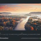 "November" steht unten. Kalenderdaten am unteren Rand. Herbstlandschaft mit Fluss und nebligem Himmel in warmen Farben.