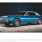 Kalender im Dezember 2027. Ein blauer, klassischer Wagen steht auf einer kiesigen Fläche unter einem sternenklaren Himmel.