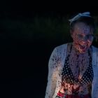 Keine sichtbaren Texte. Eine Person ist mit etwas Rötlichem bespritzt, trägt ein gepunktetes Oberteil und eine weiße Schleife.