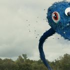 Großes Monster mit blauem Fell und großen Augen schwebt über Bäumen, umgeben von Vögeln und bewölktem Himmel.