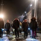 Personengruppe in Winterkleidung steht nachts vor einem großen Zug. Helle Beleuchtung, einige halten Taschenlampen.