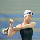 Ich kann den Text nicht erkennen. Eine Schwimmerin dehnt ihre Arme, trägt eine Badekappe und Schwimmbrille.