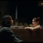 Ein Mann sitzt neben einer Badewanne, in der eine Frau entspannt. Im Hintergrund sieht man Pflanzen bei Nacht.