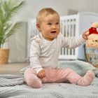 Ich kann keine Person identifizieren. Ein Baby sitzt auf einer Decke und hält ein Plüschtier in der Hand. Im Hintergrund ist ein Kinderzimmer.