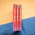 Drei Bücher mit dem Titel "The Library of Memories" stehen aufrecht. Sie haben bunte Buchrücken und ein Zeichnungslogo oben.