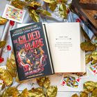 Buchcover: "The Gilded Blade" von Jennifer Lynn Barnes. Goldene Blätter, Spielkarten und eine Holztruhe als Dekoration.