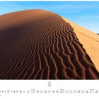 Kalenderseite mit Monatsübersicht unten, Sanddüne mittig, klare Linien im Sand und blauer Himmel.