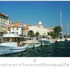“Sibenik”, “6”; Boote am Kai, historische Gebäude, kroatische Flaggen, Kuppel im Hintergrund, sonniges Wetter.