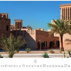 "Wind Towers in Bastakiya", eine Szene mit traditionellen Lehmgebäuden und Windtürmen unter klarem blauem Himmel.