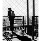 Text: "Auf dem Eiffelturm", Kalender mit Datum 1-30.  
Person mit Rucksack sieht durch Gitter über Paris. Schattenwurf.