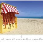 Ein Strandkorb mit rot-weißen Streifen steht am Ostseestrand. Der Himmel ist klar, das Meer blau.
