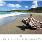 Strand von Baracoa, Kuba. Sandstrand mit totem Holz, türkisblaues Meer und bewaldete Hügel im Hintergrund.