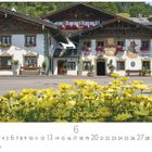 Bayrischer Dorfplatz, Frisör, Hotel Post, Weinstube. Traditionelle Gebäude mit Malereien und blühenden Blumen im Vordergrund.