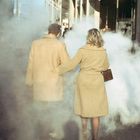 Zwei Personen in hellen Mänteln gehen Arm in Arm durch dichten Dampf. Oben sieht man das Wort "GUCCI".