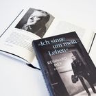 „Ich singe um mein Leben“, Reinhard Mey. Ein Porträt. Buchcover und geöffnete Buchseite mit Schwarz-Weiß-Foto.