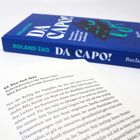 Text: "63. New York 1943" und "DA CAPO!". Ein aufgeschlagenes Buch mit gedrucktem Text; daneben ein blaues Buchcover.