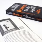 "Banksy Straße und Mythos. Eine Biografie. Reclam." Rechts liegt das Buch, links eine Seite mit Banksys Bild eines Mädchens mit Ballon.