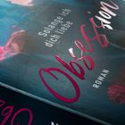 „Solange ich dich liebe“, „Obsession“, „ROMAN“. Dunkle, elegante Buchabdeckung mit rosa und blauen Blüten.