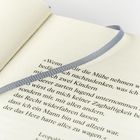 Ein geöffnetes Buch mit einem grauen Stoffleseband. Text beginnt mit „Wenn“ und endet mit „wagen.“ auf cremefarbenem Papier.
