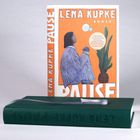 „Lena Kupke PAUSE“, Roman. Illustration: Person im Pyjama mit Tasse, Pflanze, oranger Hintergrund.