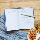 Offenes Notizbuch mit Fragen zur Musikauswahl, Stift, Snacks und Stoff auf Holzuntergrund.