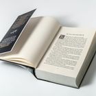 Aufgeschlagenes Buch mit dem Kapitel „Una und die Eibe“. Daneben ein schwarzer Einband mit weißem Text.