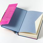 Ein aufgeschlagenes Buch mit einer pinken Seite, die weißen Text enthält. Die Buchseiten sind blau und cremeweiß.