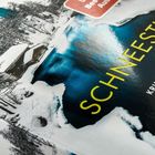 "SchNEEStILL" und "KRIMINALROMAN" stehen auf einem Buchcover mit schneebedeckter Hütte am blauen See.