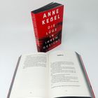 Ein aufgeschlagenes Buch zeigt "Kapitel 23" auf Seite 156/157. Ein rotes Buchcover mit "ANNE KEBEL DIE LÜGE IN IHREM GESICHT".