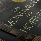 "Das Monument der Hoffnung" steht in großen Buchstaben auf einem Buchcover, begleitet von dekorativen Mustern.