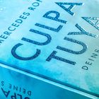 Text: "Culpa Tuya", "Deine Schuld", "Mercedes Ron". Glitzernde blaue Schrift auf einem türkisen Buchcover.