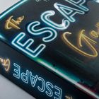 "The Escape Game" in leuchtenden Buchstaben, eine Nahaufnahme eines Buchrückens in Neonfarben.