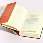 Ein Buch mit orangem Umschlagtext, geöffnet. Zitate von Joan Didion und Erri De Luca. Hellgelbe Seiten.