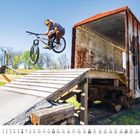 Text unten: "6", Datumskontext. Ein Radfahrer springt von einer Rampe vor einem alten, rostigen Güterwaggon.