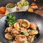 Ein schwarzer Teller mit gebratenen Gnocchi, mit Petersilie und gehackten Nüssen, daneben Soßen in weißen Schälchen.